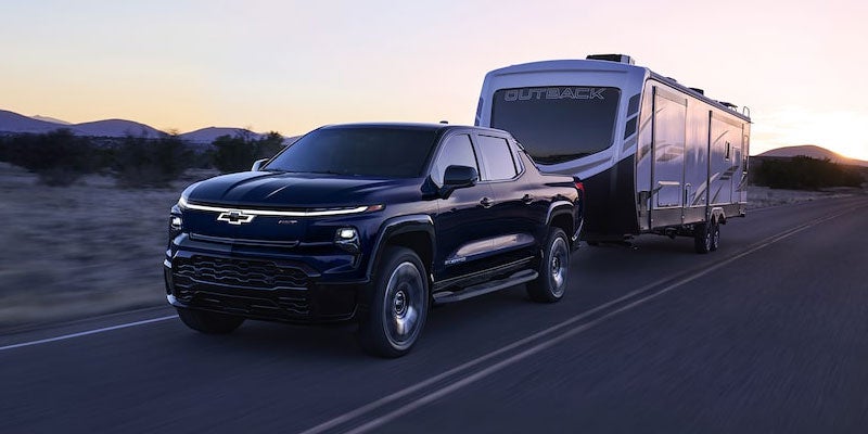 A 2021 Chevrolet Silverado towing a camper on a scenic road.